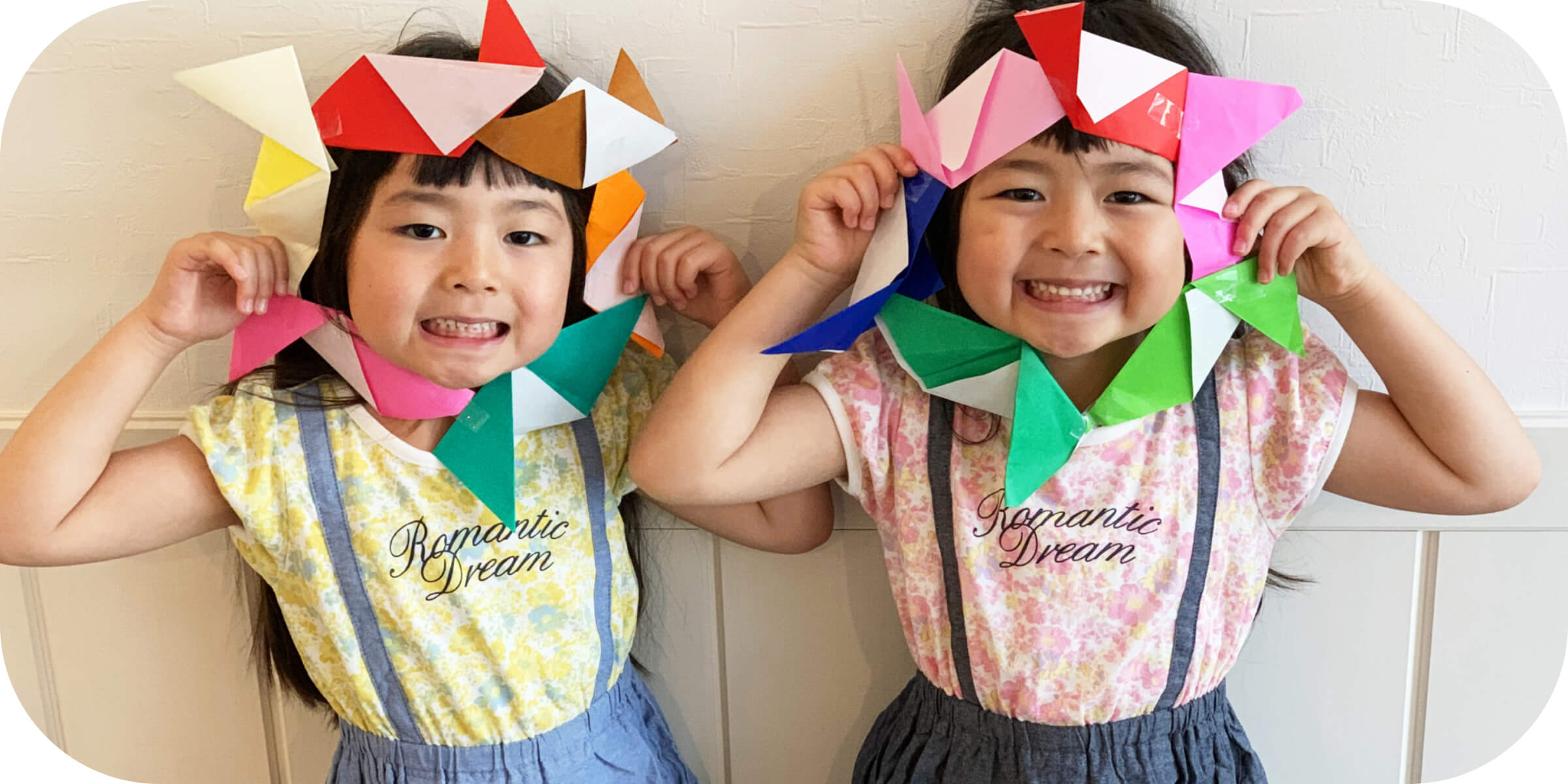 二人の女の子が折り紙で作った輪を顔に当てて笑っている。
